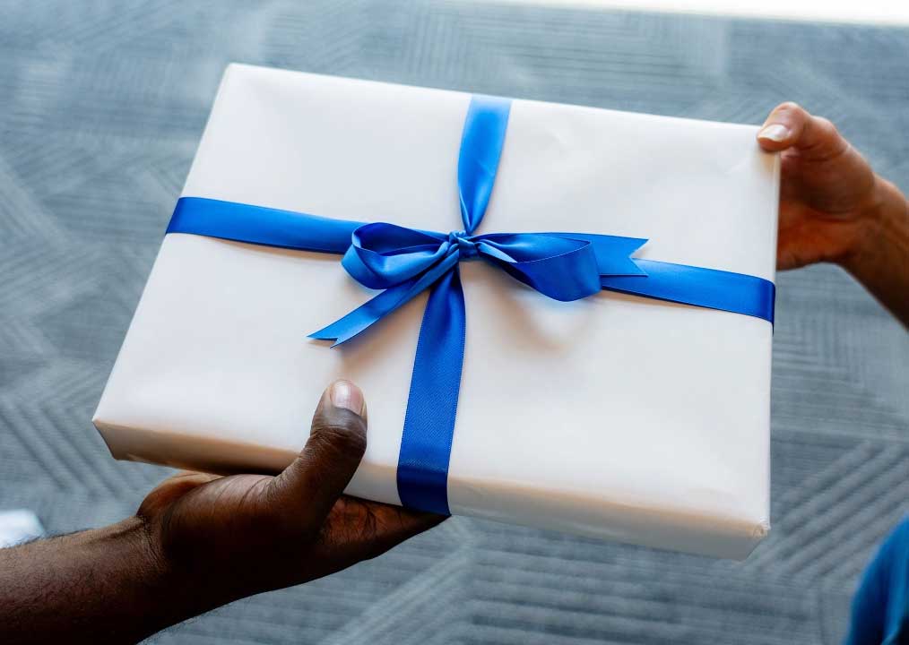 Hands holding a white gift box tied with a blue ribbon