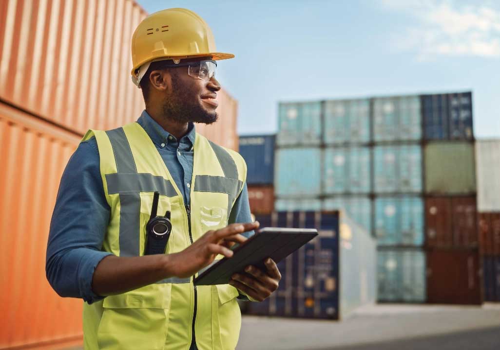 Warehouse worker in a hard hat and safety vest holding a tablet